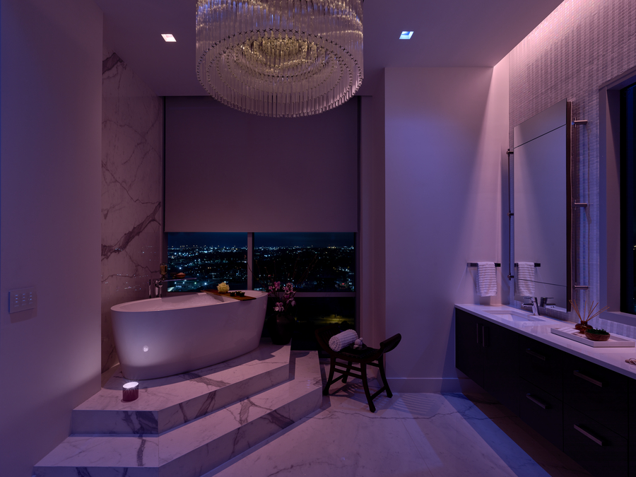 A bathroom with a soaking tub illuminated in Lutron Ketra’s lavender lighting with shades partially drawn. 